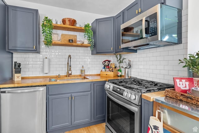 kitchen featuring stainless steel appliances, a sink, open shelves, decorative backsplash, and wooden counters
