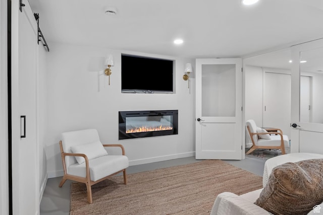living area with a glass covered fireplace, a barn door, recessed lighting, and baseboards