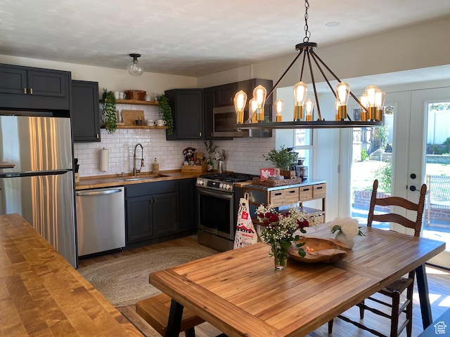 kitchen featuring appliances with stainless steel finishes, a sink, wooden counters, decorative backsplash, and light wood-type flooring