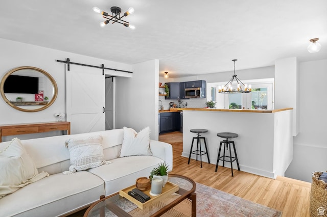 living area with a chandelier, a barn door, light wood-style floors, and baseboards