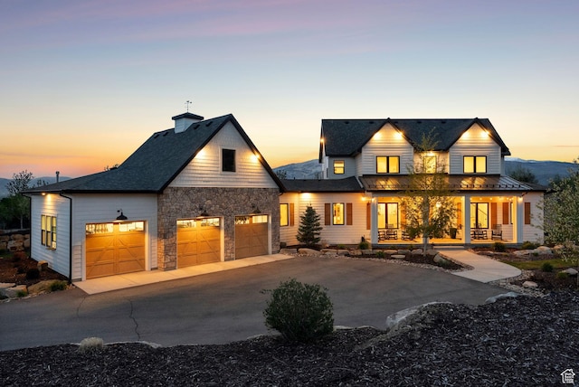 1677 Lambert Ln, Kamas, UT 84036 - view of front facade featuring a porch, concrete driveway, stone siding, a chimney, and a garage