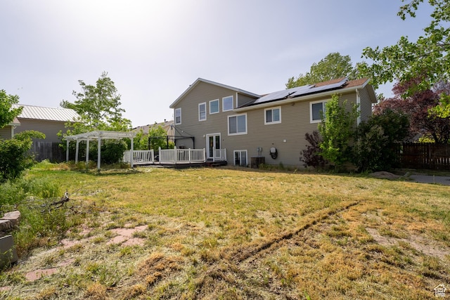 back of property featuring a pergola, a wooden deck, and roof mounted solar panels