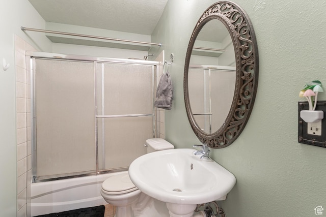 bathroom with a sink, toilet, enclosed tub / shower combo, and a textured wall