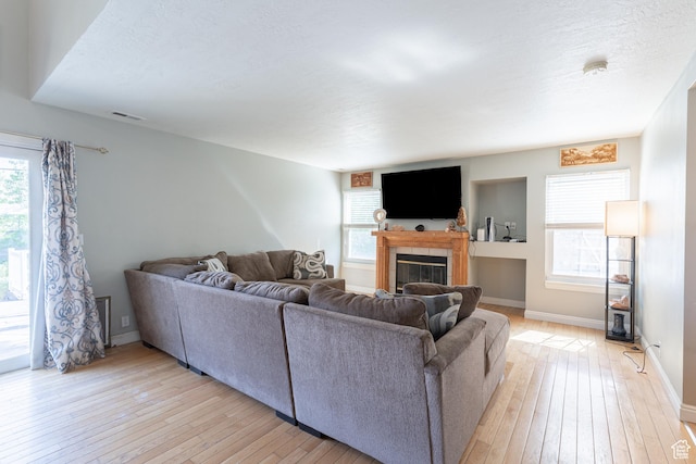 living area with light wood-type flooring, a fireplace, plenty of natural light, and baseboards