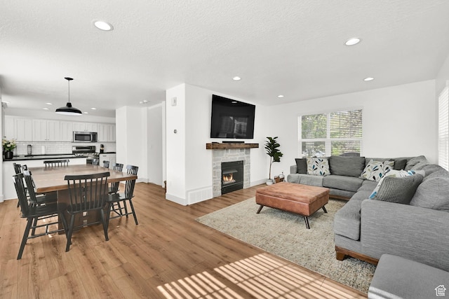 3553 N Willow Creek Ln E, Eden, UT 84310 - living room featuring recessed lighting, light wood-type flooring, a stone fireplace, baseboards, and a textured ceiling