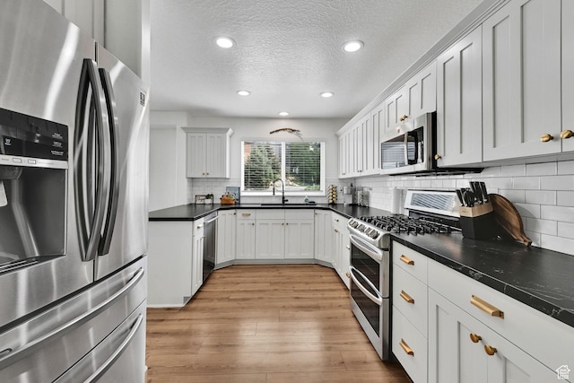 3553 N Willow Creek Ln E, Eden, UT 84310 - kitchen featuring stainless steel appliances, light wood-style flooring, a textured ceiling, decorative backsplash, and dark countertops