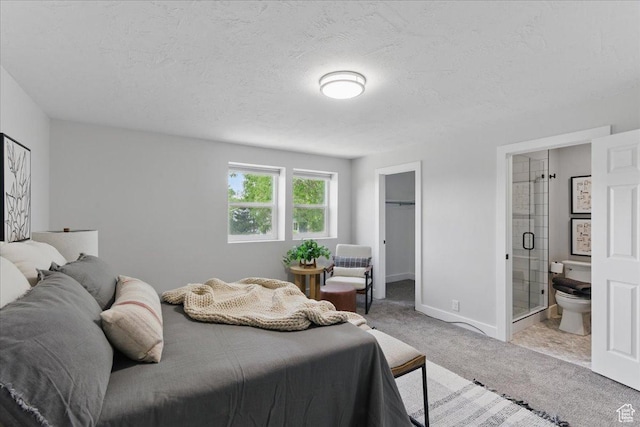 bedroom with carpet flooring, a spacious closet, a textured ceiling, ensuite bath, and baseboards