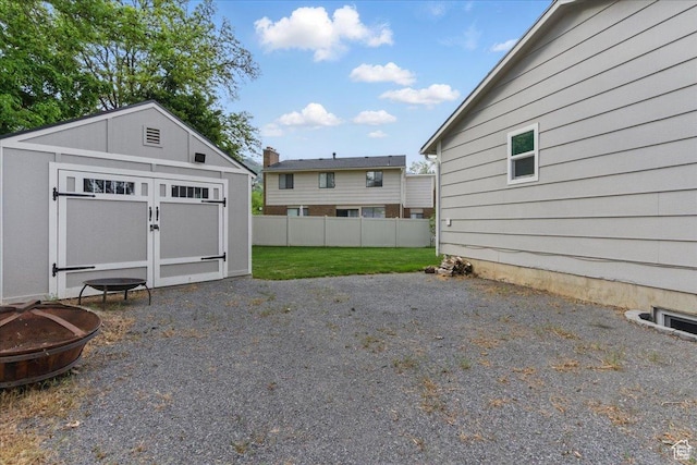 view of yard with a fire pit, a storage shed, fence, and an outbuilding