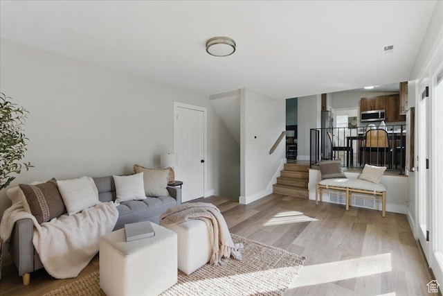 living room featuring light wood-type flooring, stairway, and baseboards
