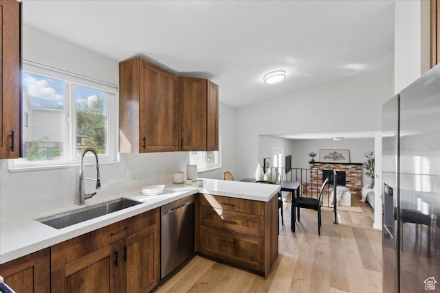 kitchen with appliances with stainless steel finishes, a sink, a peninsula, light wood-type flooring, and light countertops