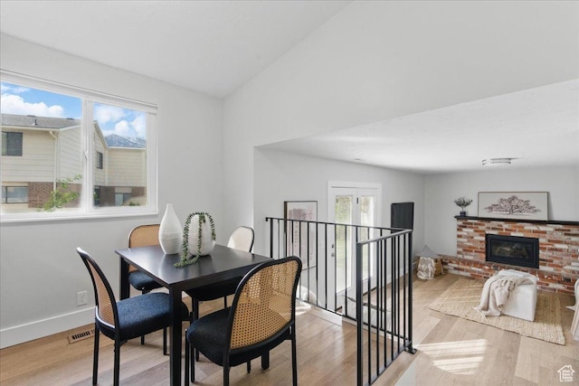 dining room featuring light wood-type flooring, plenty of natural light, a fireplace, baseboards, and lofted ceiling