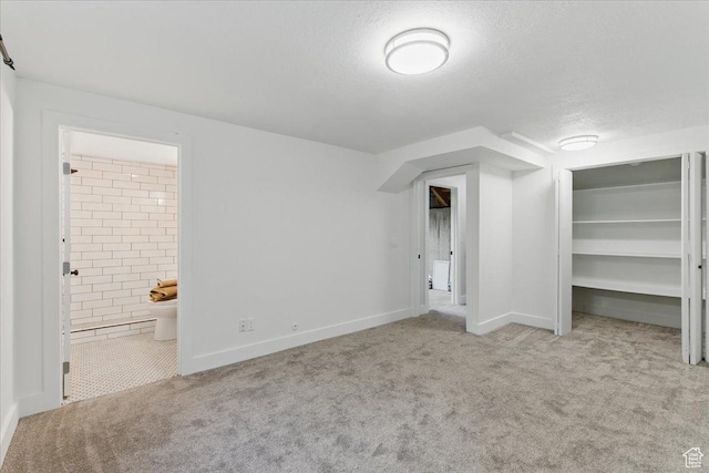 unfurnished bedroom with carpet floors, a textured ceiling, ensuite bathroom, baseboards, and a closet