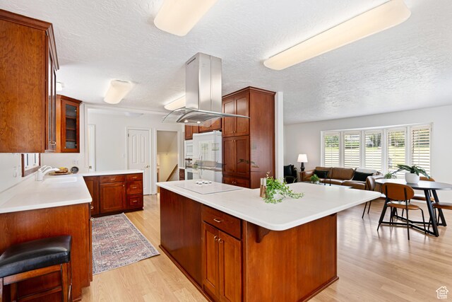 4115 Edgehill Dr, Ogden, UT 84403 - kitchen featuring island exhaust hood, light wood finished floors, a center island, glass insert cabinets, and a textured ceiling