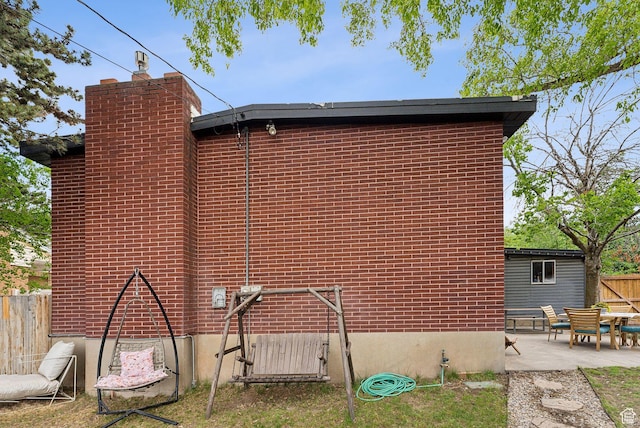 32 S Kingdon Ln E, North Salt Lake, UT 84054 - view of home's exterior featuring fence, a patio area, a chimney, and brick siding