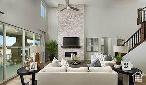 living area featuring a towering ceiling, a ceiling fan, healthy amount of natural light, a large fireplace, and wood finished floors