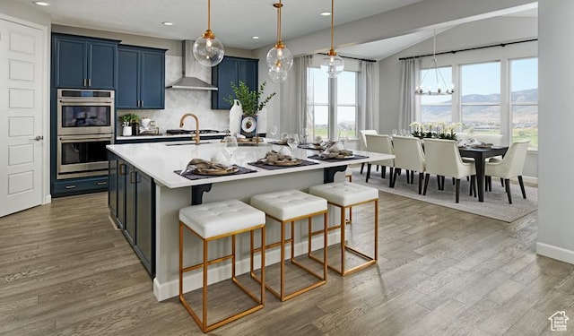 kitchen featuring double oven, wall chimney range hood, blue cabinetry, a mountain view, and a chandelier