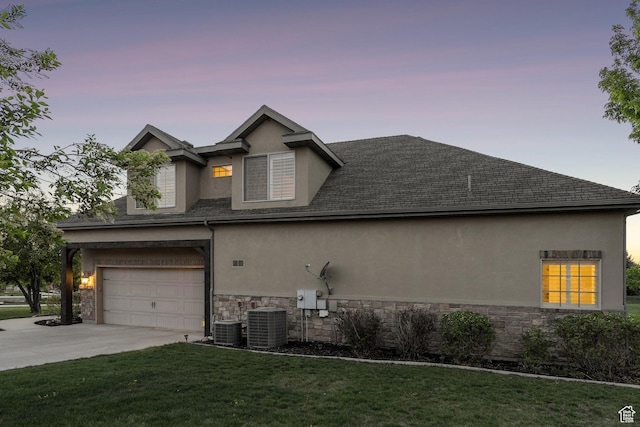 property exterior at dusk with stucco siding, stone siding, driveway, cooling unit, and a yard