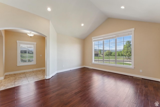 spare room with arched walkways, healthy amount of natural light, wood finished floors, vaulted ceiling, and baseboards