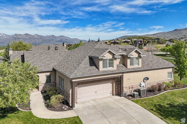 view of front facade featuring stucco siding, stone siding, driveway, a mountain view, and a garage