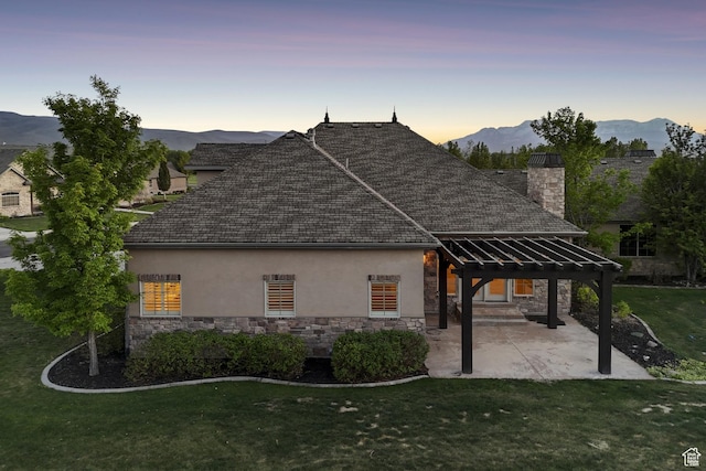 property exterior at dusk featuring stone siding, a pergola, stucco siding, and a yard