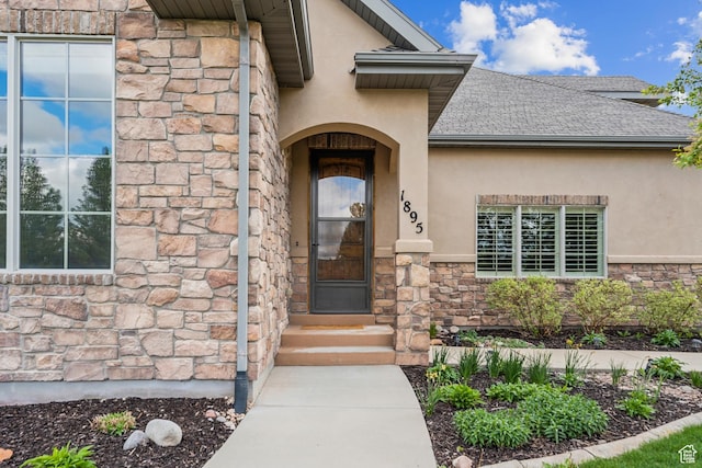 doorway to property with stucco siding, stone siding, and a shingled roof