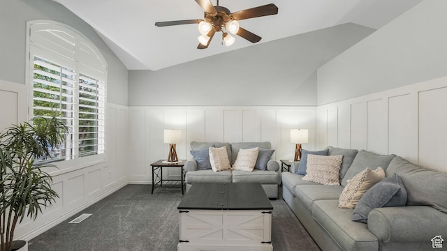 living area featuring a decorative wall, ceiling fan, carpet flooring, vaulted ceiling, and wainscoting