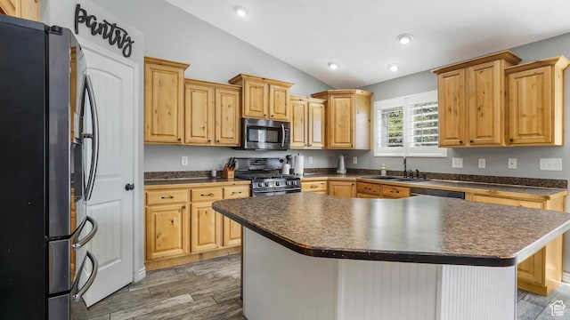 kitchen featuring appliances with stainless steel finishes, dark countertops, vaulted ceiling, a sink, and light wood-type flooring