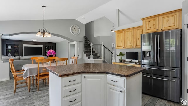 kitchen featuring stainless steel fridge with ice dispenser, lofted ceiling, dark countertops, arched walkways, and wood finished floors