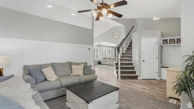 living area featuring arched walkways, a ceiling fan, stairway, wood finished floors, and a wainscoted wall