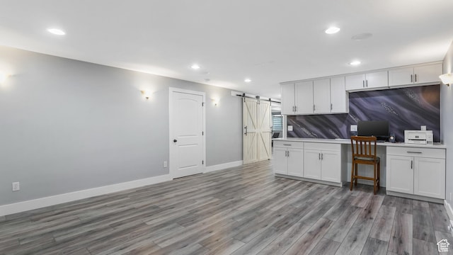 kitchen with a barn door, wood finished floors, recessed lighting, baseboards, and white cabinetry