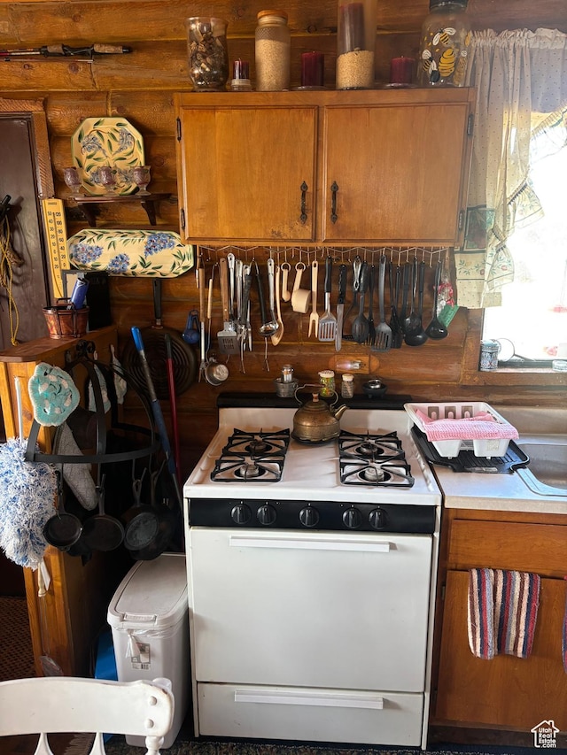 kitchen with white gas range oven, brown cabinets, and light countertops