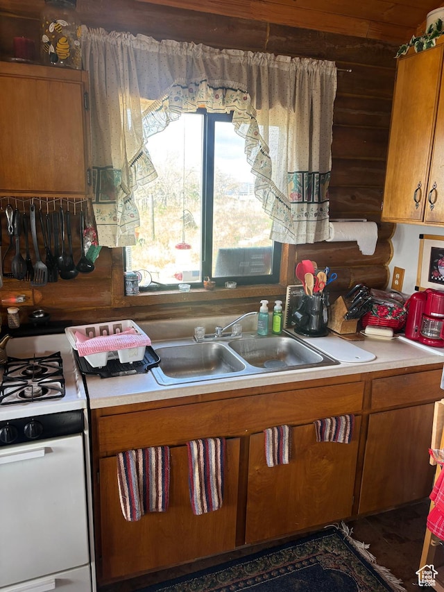 kitchen with brown cabinets, light countertops, a sink, and range with gas cooktop