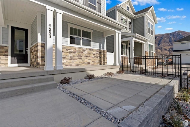 doorway to property featuring a porch, stone siding, fence, and a mountain view