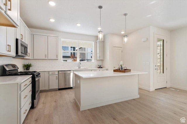 kitchen featuring appliances with stainless steel finishes, a sink, light wood-style flooring, decorative backsplash, and light countertops