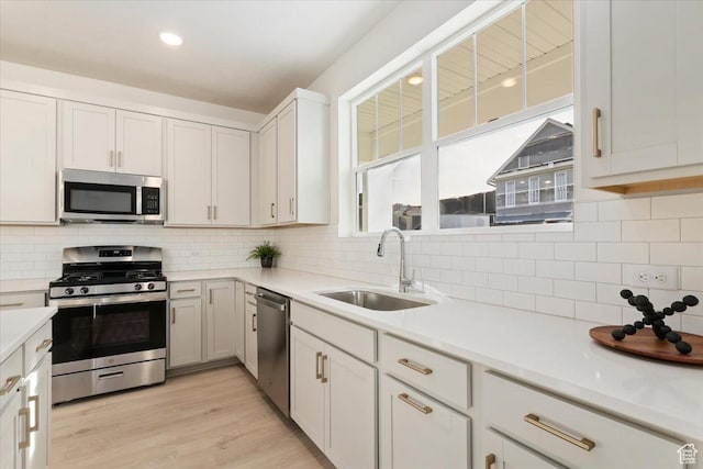 kitchen with appliances with stainless steel finishes, a sink, backsplash, light countertops, and light wood finished floors