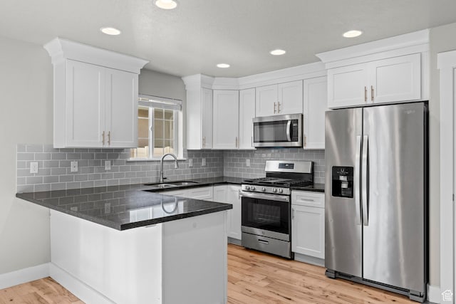 kitchen featuring appliances with stainless steel finishes, a sink, a peninsula, white cabinetry, and light wood finished floors