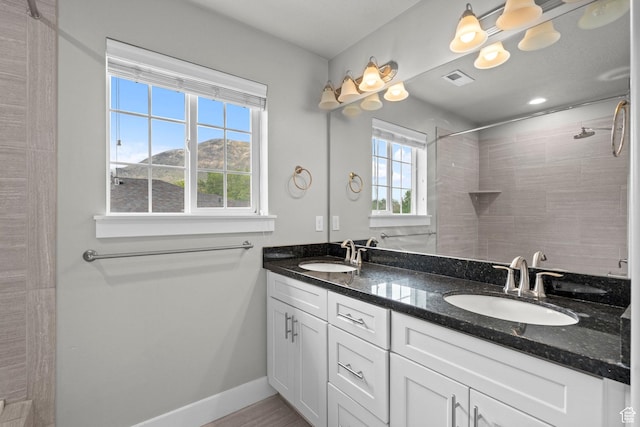 full bathroom featuring double vanity, a tile shower, and baseboards
