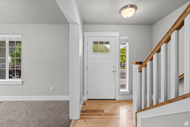 entrance foyer featuring a textured ceiling, stairs, plenty of natural light, hardwood / wood-style flooring, and baseboards