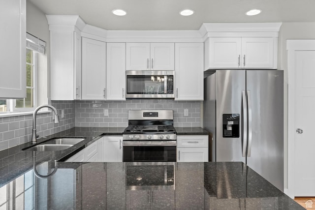 kitchen featuring appliances with stainless steel finishes, a sink, white cabinets, dark stone countertops, and recessed lighting