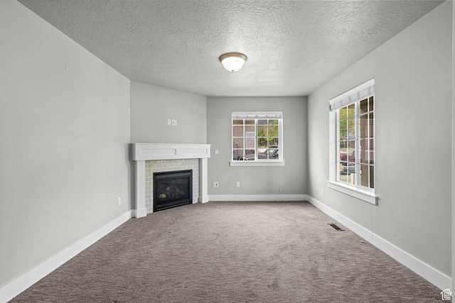 unfurnished living room with a textured ceiling, carpet, a brick fireplace, and baseboards