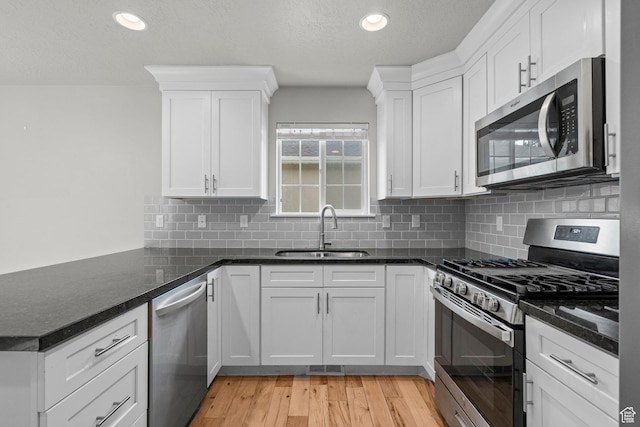 kitchen featuring appliances with stainless steel finishes, a sink, a peninsula, white cabinets, and recessed lighting