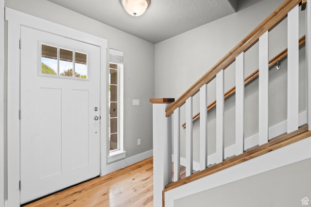 entryway with light wood-style flooring, a textured ceiling, and baseboards