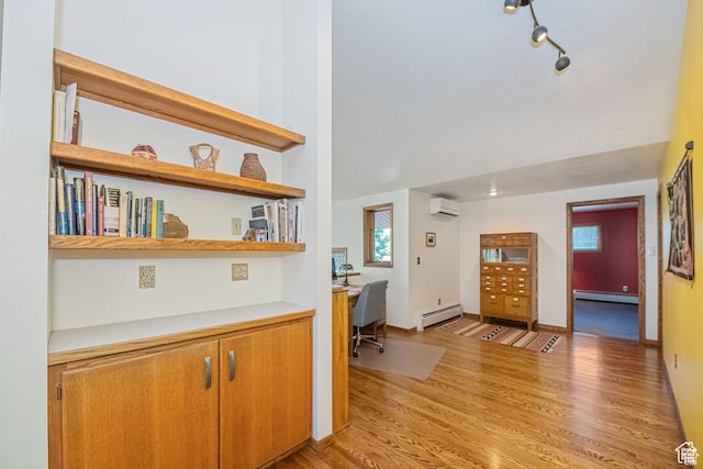 entryway with a baseboard radiator, a wall mounted AC, built in study area, light wood-style flooring, and a towering ceiling