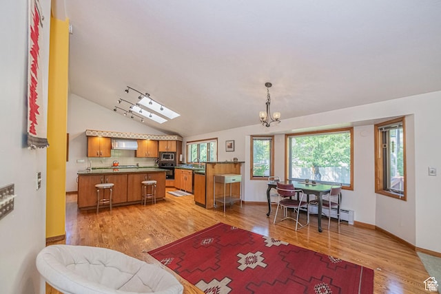 kitchen with brown cabinets, stainless steel microwave, dark countertops, light wood finished floors, and wall chimney range hood