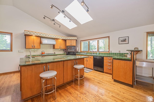 kitchen featuring stainless steel appliances, a skylight, vaulted ceiling, wall chimney range hood, and a sink