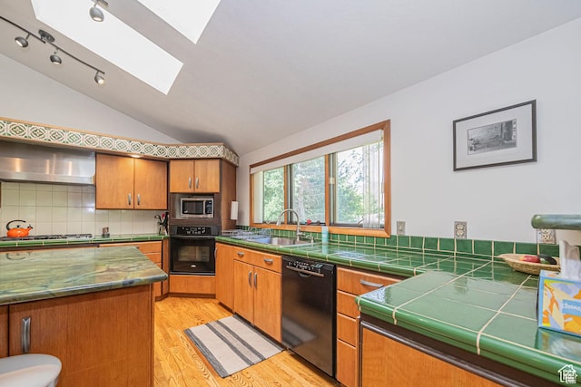 kitchen with black appliances, a sink, a skylight, vaulted ceiling, and light wood-style flooring