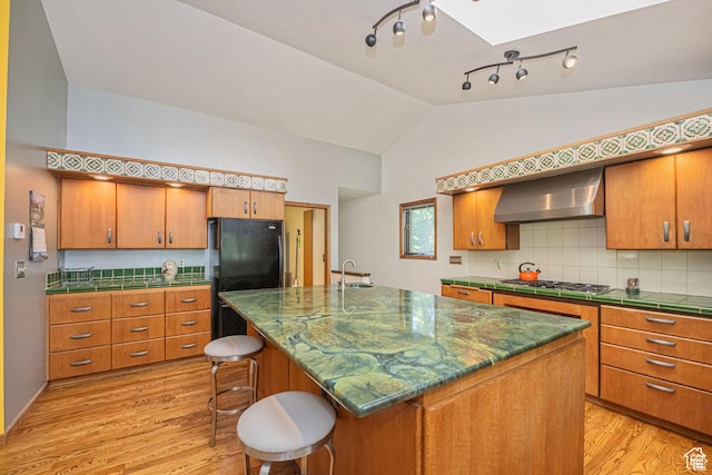 kitchen with wall chimney exhaust hood, light wood-type flooring, stainless steel gas stovetop, a skylight, and lofted ceiling