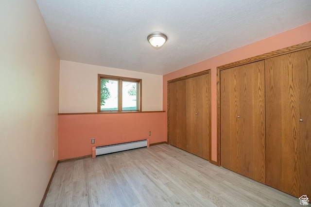 unfurnished bedroom featuring baseboard heating, light wood finished floors, two closets, and baseboards