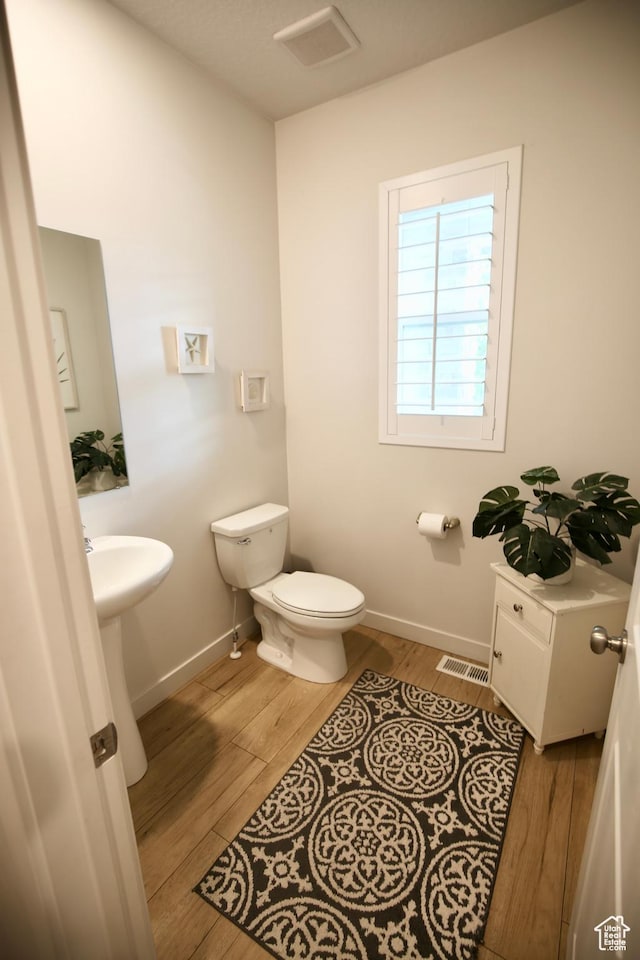 half bathroom featuring toilet, wood finished floors, baseboards, and a sink