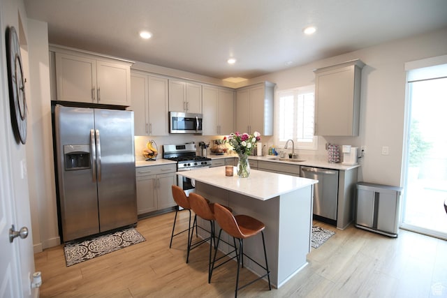 kitchen with stainless steel appliances, gray cabinets, a sink, light wood-style flooring, and a breakfast bar